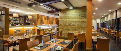 Un restaurante moderno con mesas y sillas de madera, una zona de bar y una pared de piedra.
