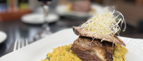 Un plato de comida con un trozo de carne y un puré amarillo, servido en un plato blanco con borde decorativo.