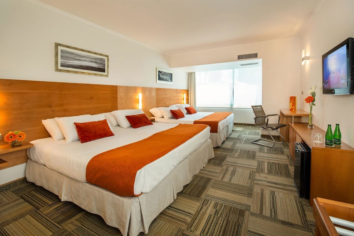 A hotel room with two beds, a desk, a chair, a TV, and a window.
