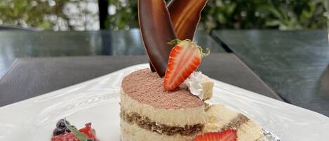 Un postre en un plato blanco con fresas, arándanos y trozos de chocolate.