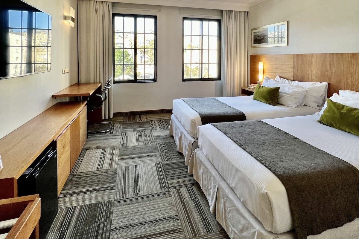 A hotel room with two beds, a desk, a chair, a TV, and a window with curtains.