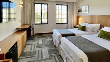 Habitación de hotel con dos camas, un escritorio, una silla, un televisor y una ventana con cortinas.