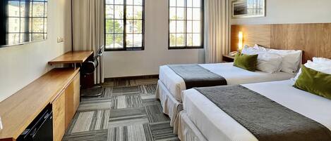 A hotel room with two beds, a desk, a chair, a TV, and a window with curtains.