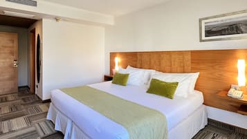 Habitación de hotel con una cama grande, cabecera de madera, mesita de noche con lámpara y un cuadro enmarcado en la pared.