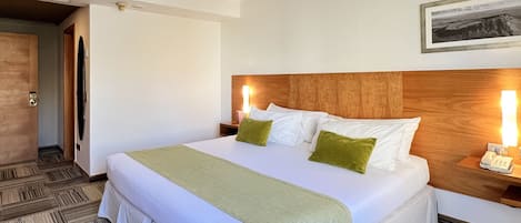 Habitación de hotel con una cama grande, cabecera de madera, mesita de noche con lámpara y un cuadro enmarcado en la pared.