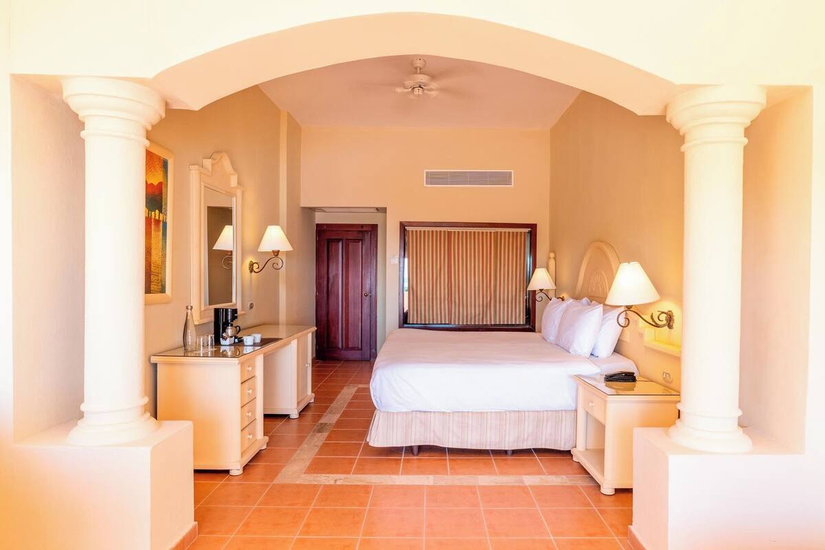Ein Hotelzimmer mit einem Bett, Nachttischen, einem Schminktisch, einem Spiegel und einem Deckenventilator.