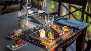 A dining table with a steak, roasted potatoes, and a small dish of sauce. There are also two wine glasses and a glass of water.