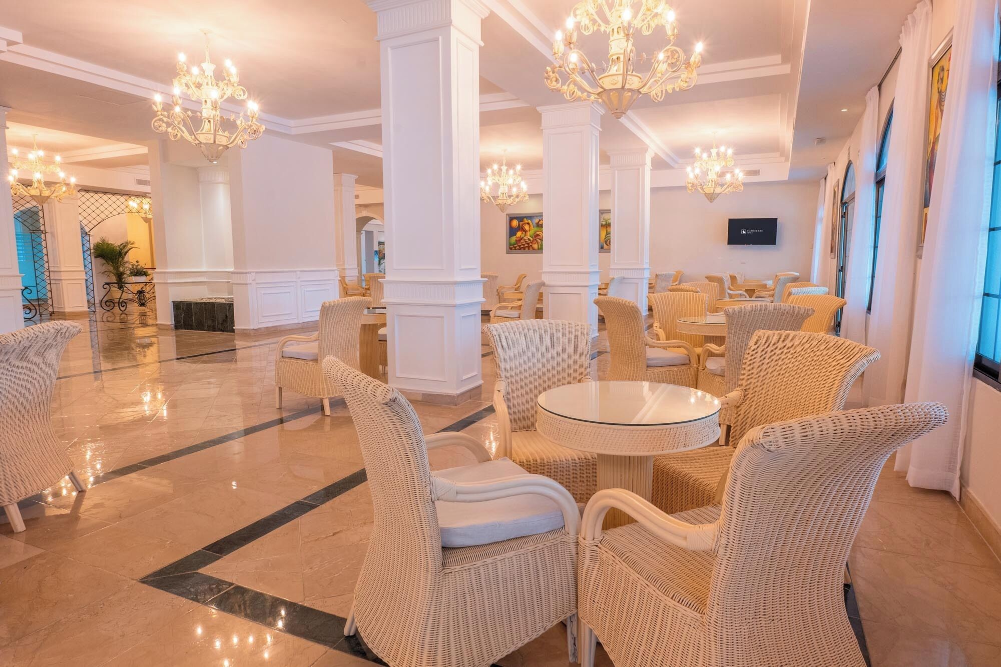 A spacious lobby with high ceilings, ornate chandeliers, and wicker furniture.