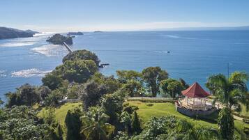 A coastal view with a gazebo, lush greenery, and a bridge over the water.