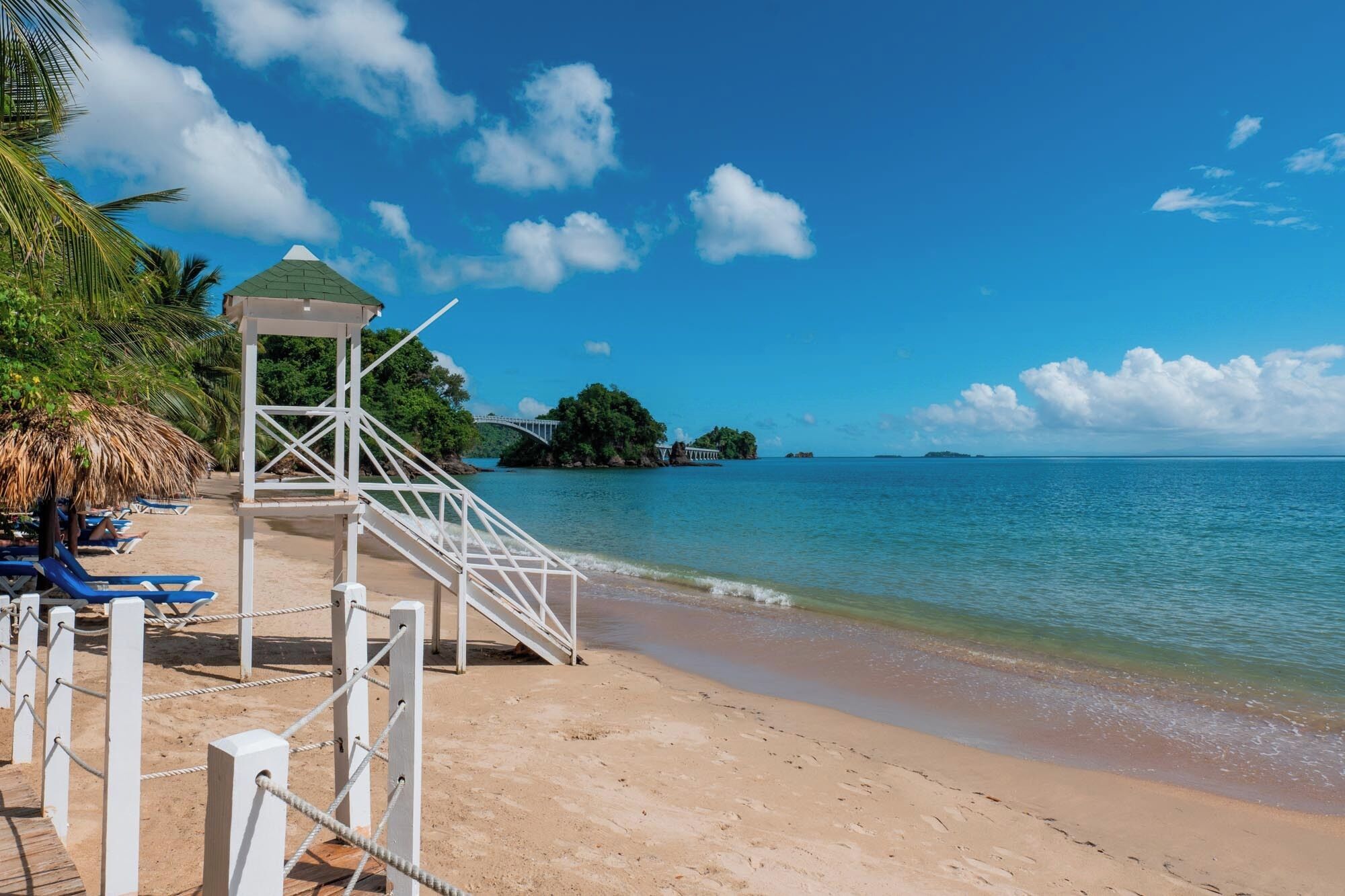 Une plage avec un kiosque blanc, des chaises longues bleues et une rive sablonneuse.