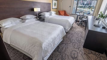 Une chambre d’hôtel avec deux lits, un bureau, une chaise et une grande fenêtre donnant sur la ville.