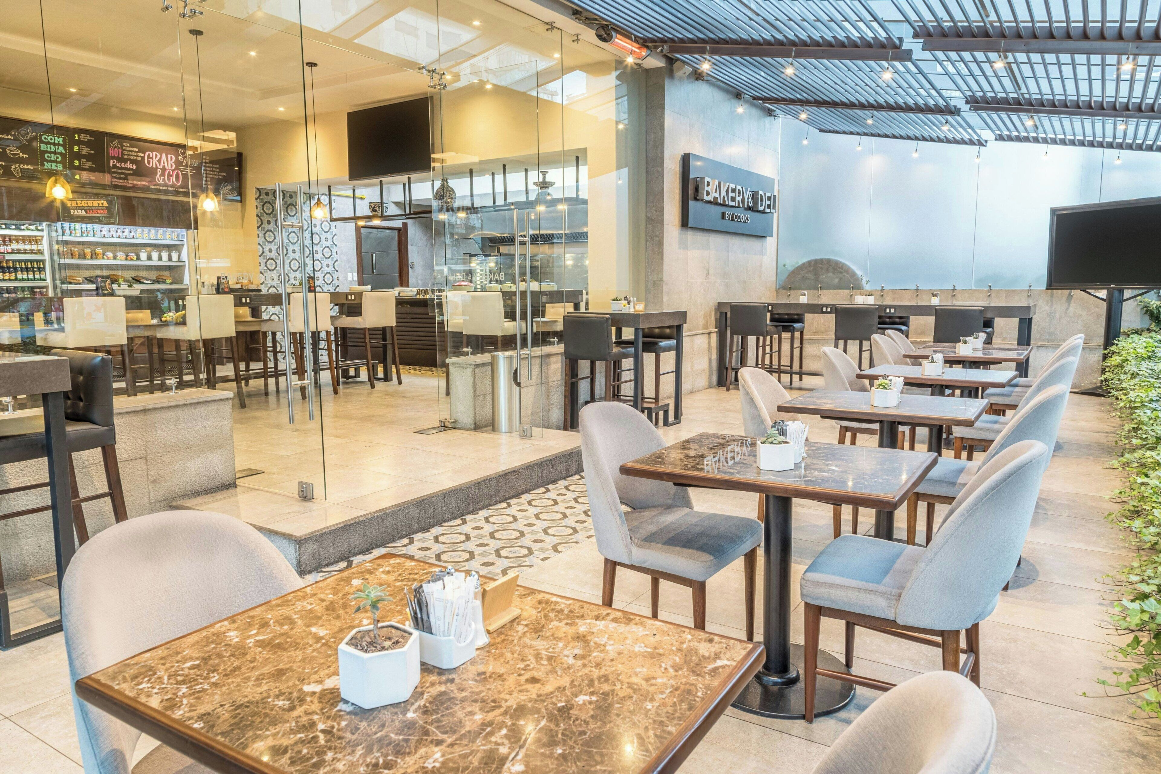 Un restaurante moderno con mesas y sillas de mármol, una zona de cocina a la vista y una pizarra con la carta.