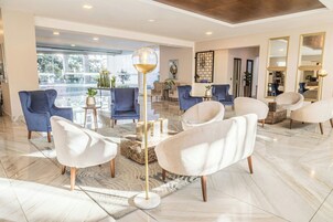 A modern lobby with a marble floor, blue and white armchairs, a glass coffee table, and a gold floor lamp.