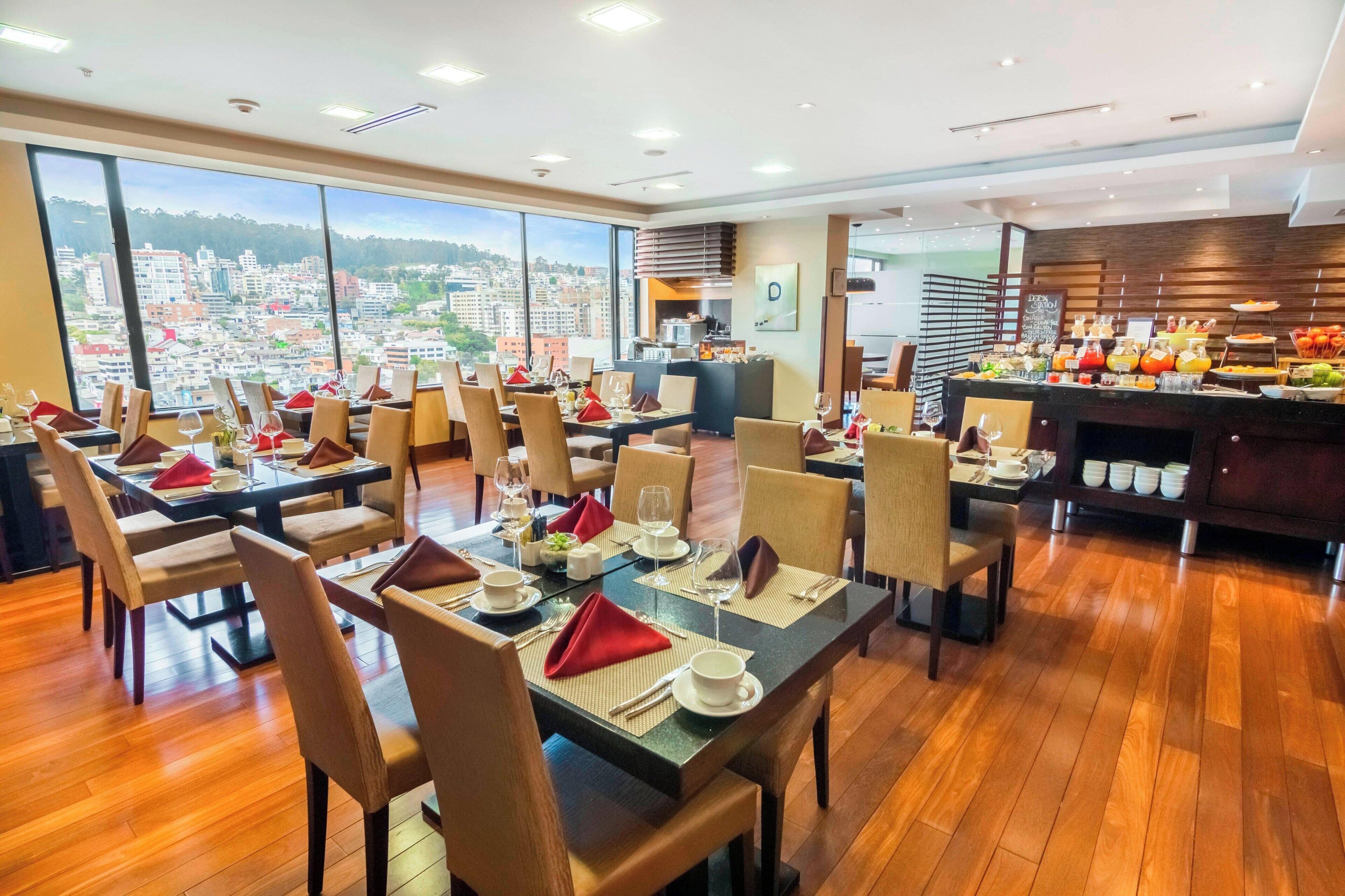 Um restaurante com várias mesas preparadas, com guardanapos vermelhos, pratos brancos e copos.