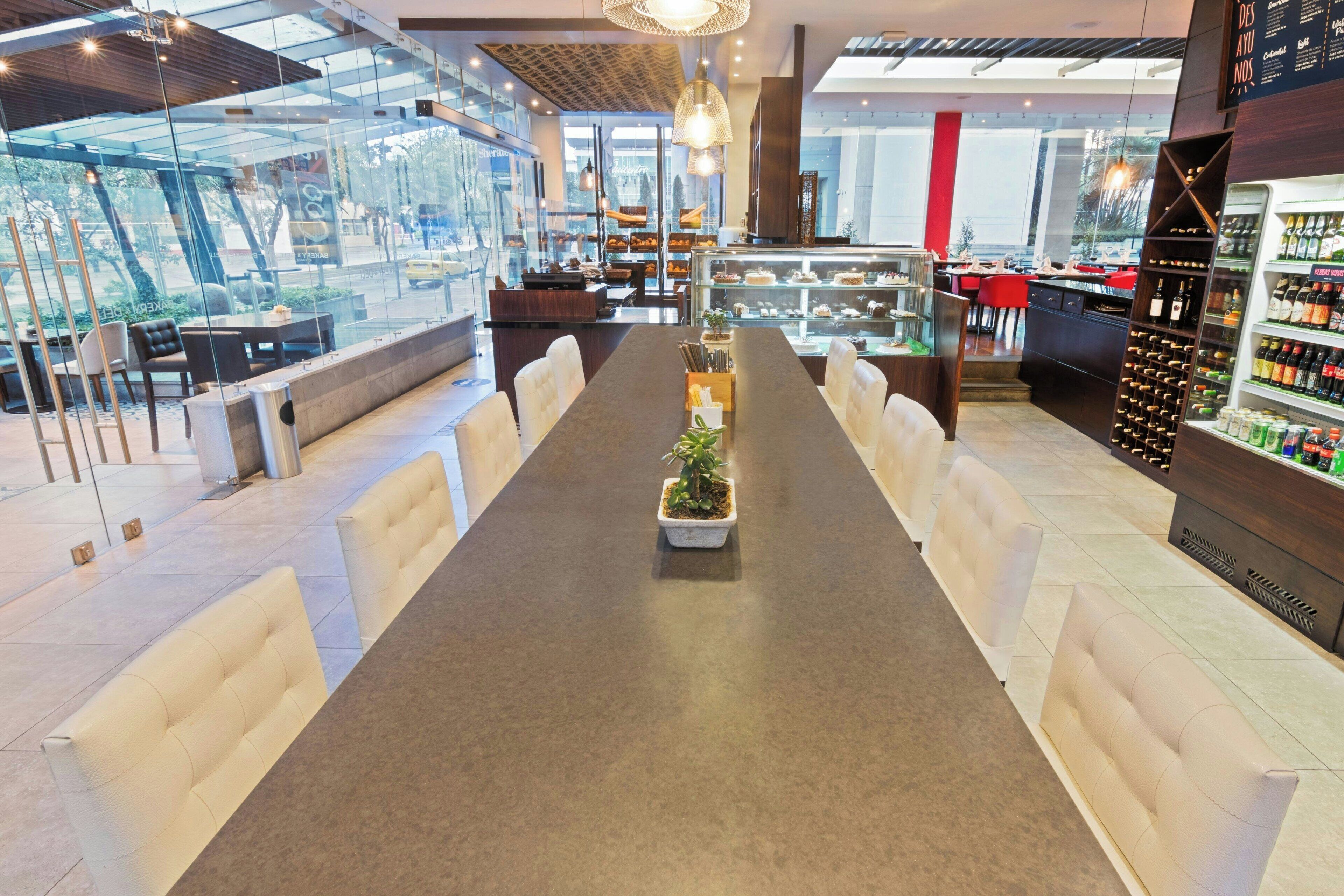 Un restaurant moderne avec une longue table à manger, des chaises blanches rembourrées, une plante au centre et un meuble à vin.