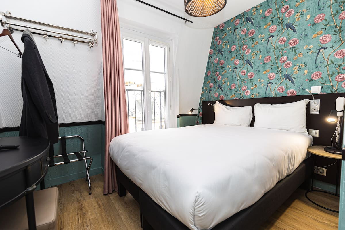 A hotel room with a bed, a desk, a chair, a window, and a curtain.