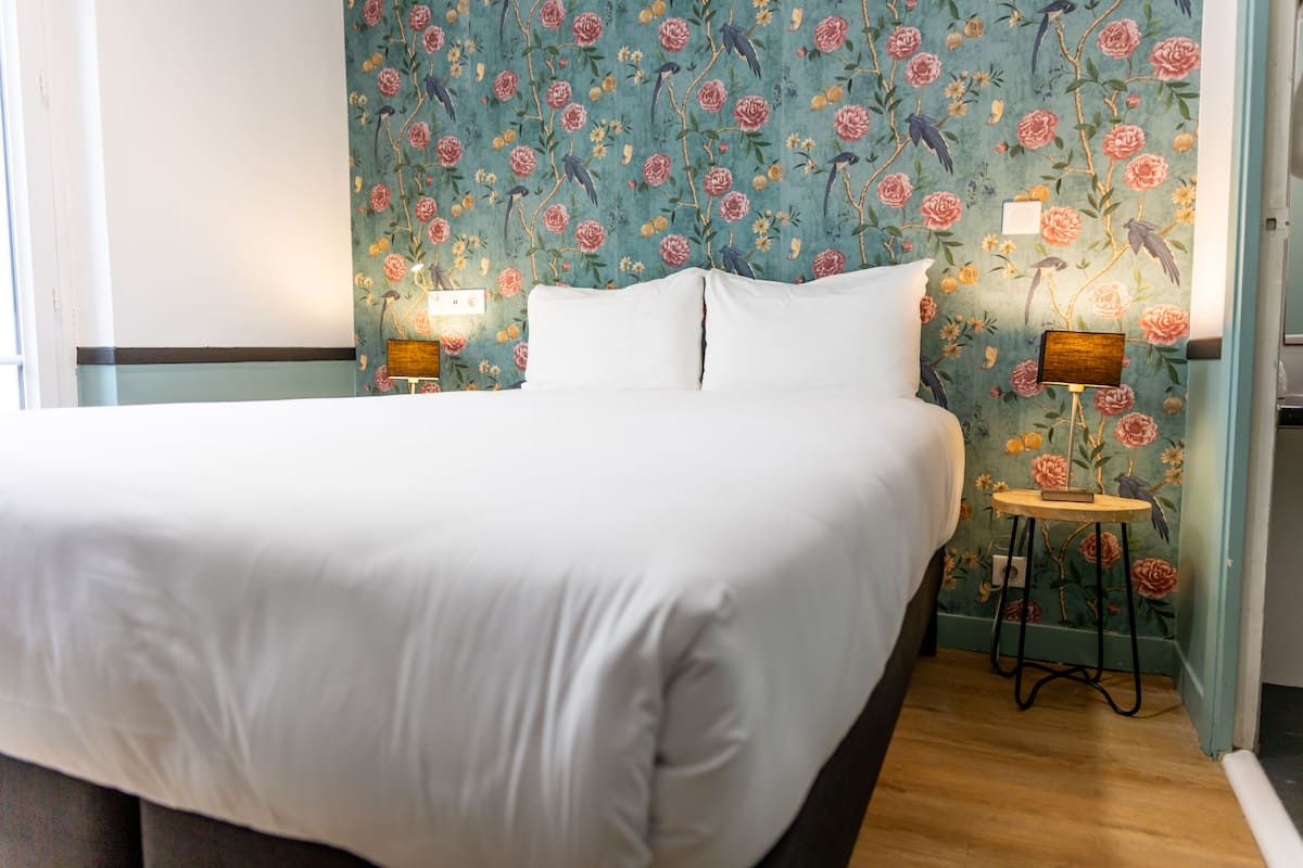 A neatly made bed with white linens, a floral wallpaper pattern, and two bedside lamps on wooden nightstands.