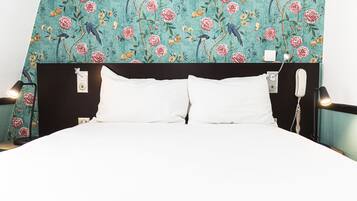 Un lit avec du linge de lit blanc, une tête de lit sombre et un mur orné d’un motif floral.