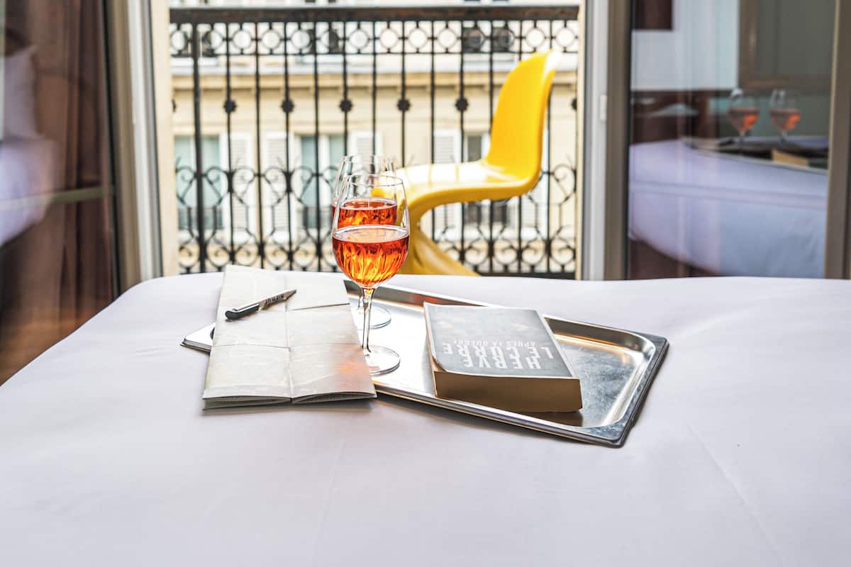 A hotel room with a balcony, a dining table with a glass of wine, a book, and a tray.