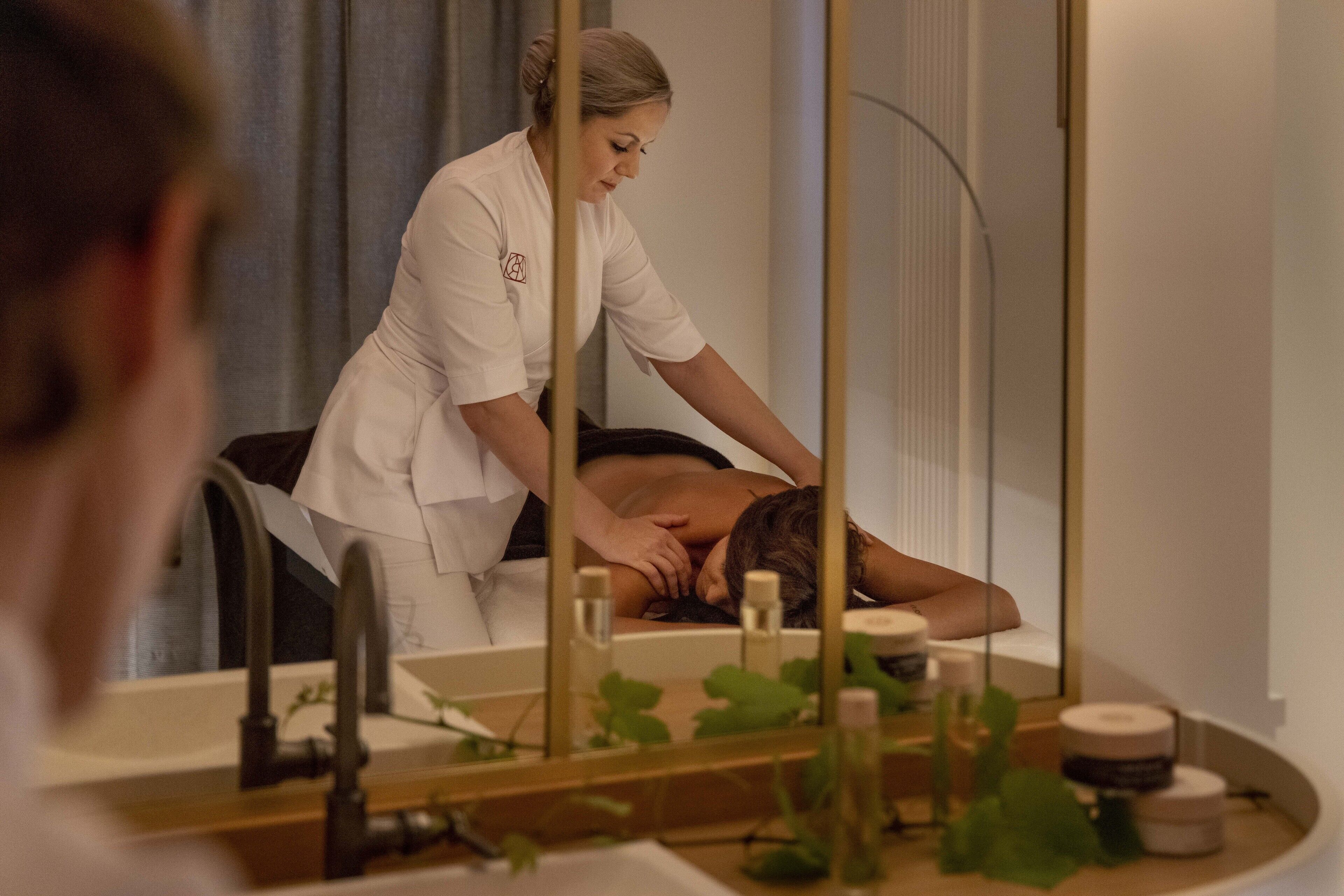 A spa setting with a person receiving a massage, a mirror, and various spa products on the counter.
