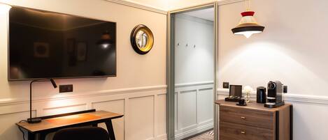A hotel room with a flat-screen TV, a desk with a chair, a dresser, and a patterned carpet.