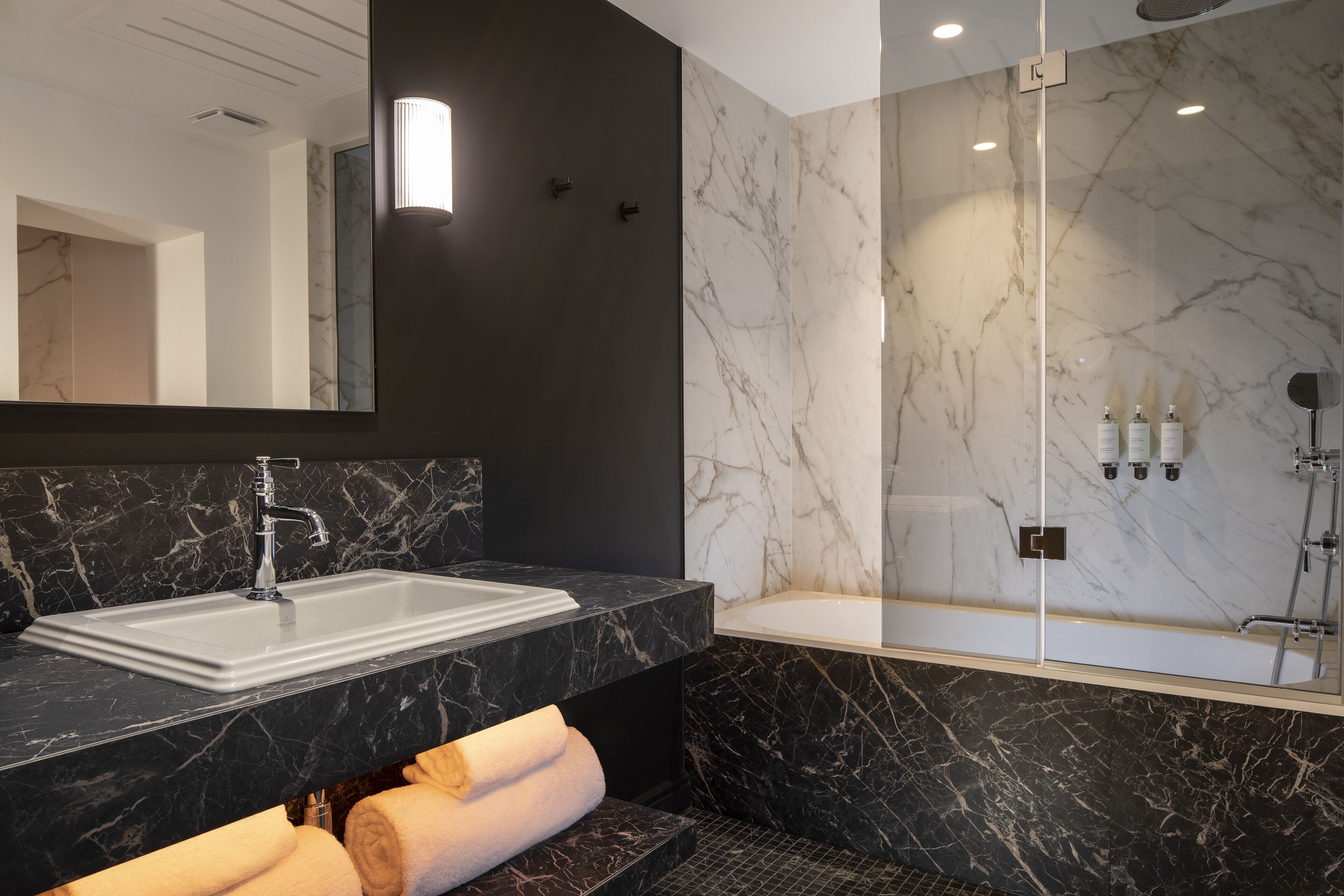 Un baño moderno con lavamanos de mármol negro, un espejo grande y cabina de ducha con paredes de vidrio.