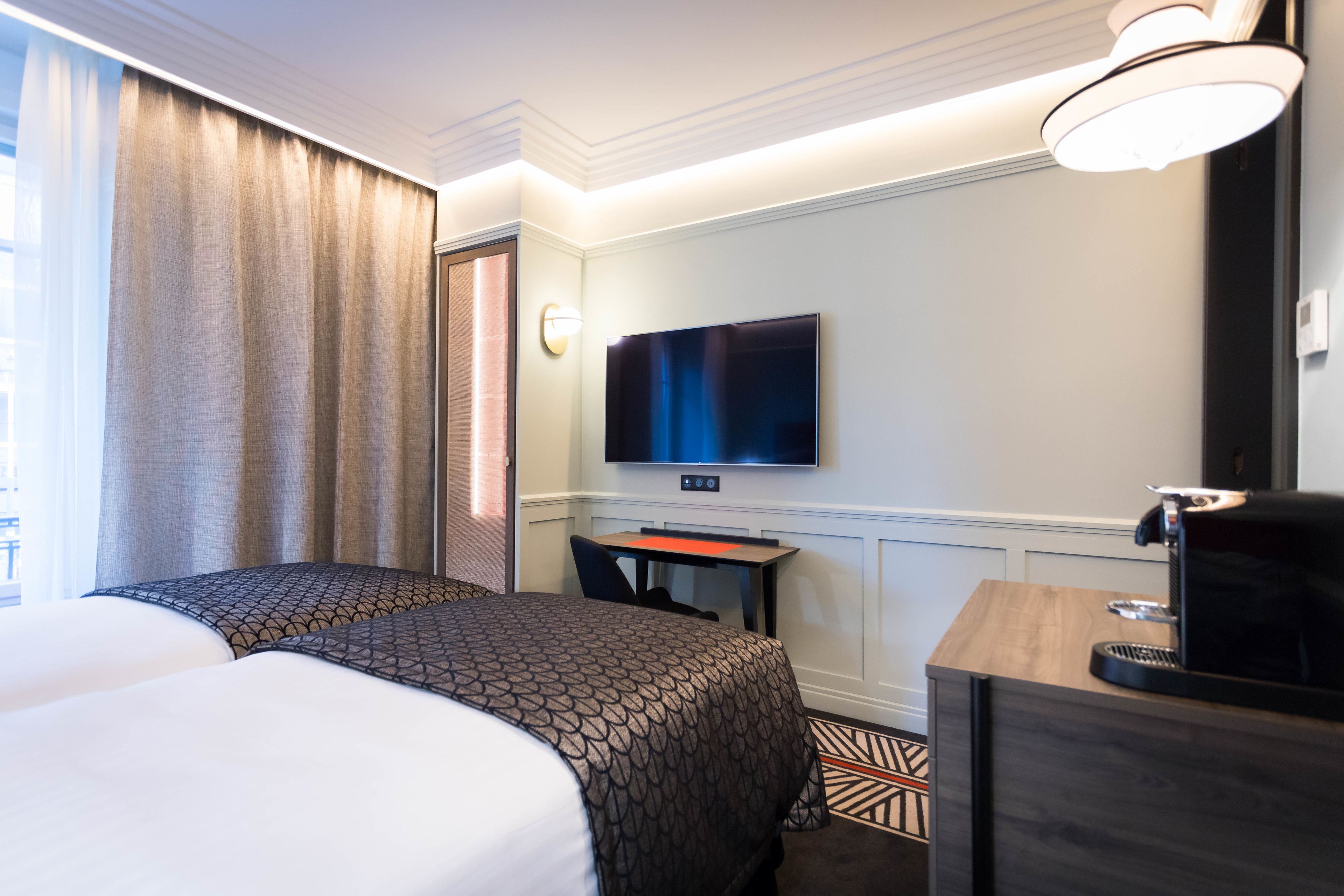 Habitación de hotel con dos camas, un escritorio, un televisor y una cafetera.