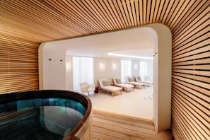 Un espace spa moderne doté d’un plafond en lambris de bois, d’un jacuzzi et d’un coin salon avec des fauteuils et un canapé.