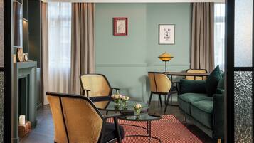 A living room with a fireplace, two wicker chairs, a round table with vases, a green sofa, and a patterned rug.