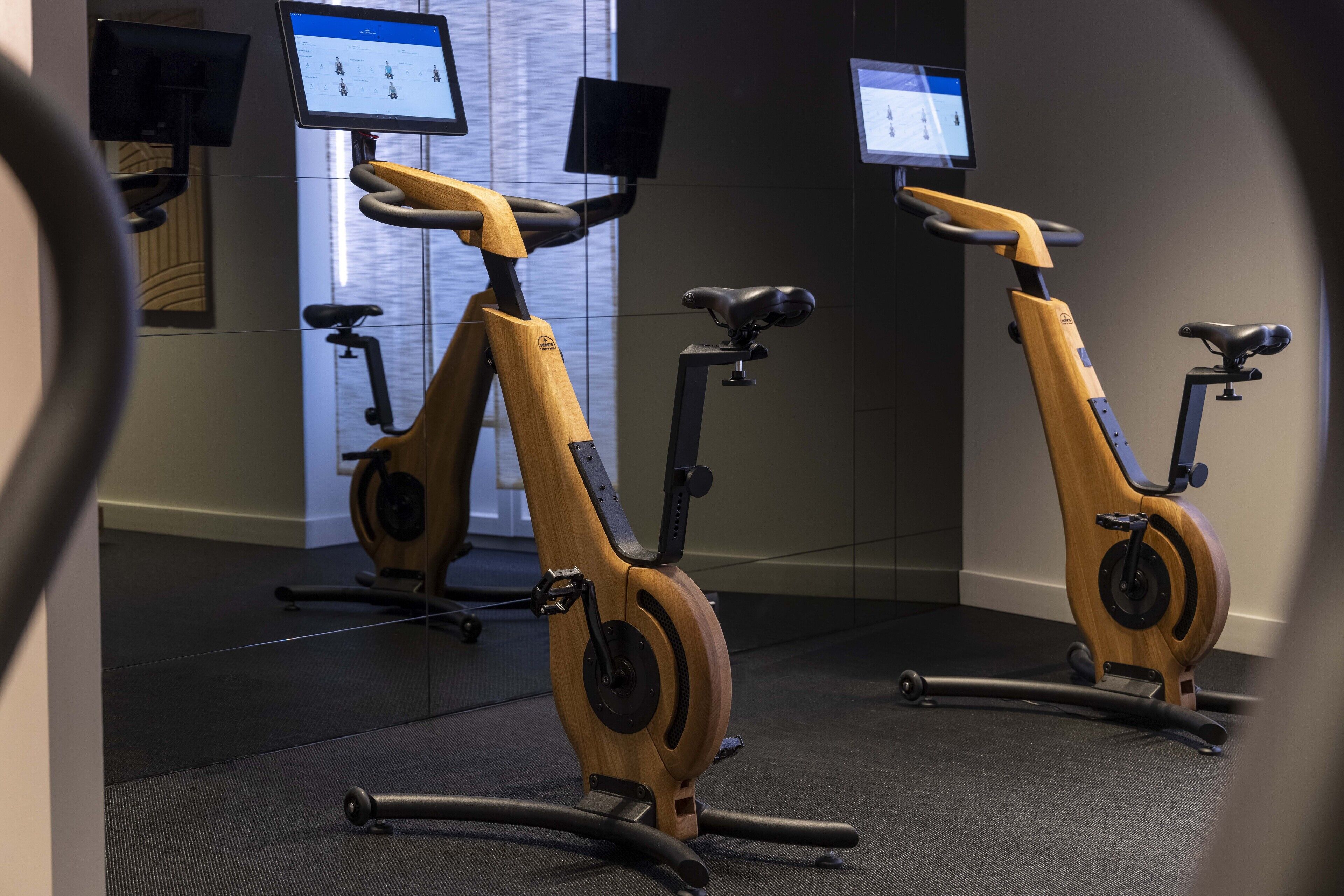 Two stationary bikes in a room with mirrored walls and screens displaying content.