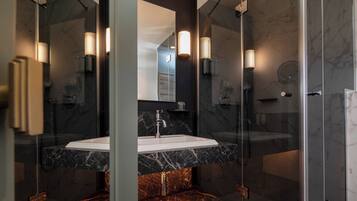 Un baño moderno con cabina de ducha de vidrio, lavamanos de mármol e iluminación empotrada.