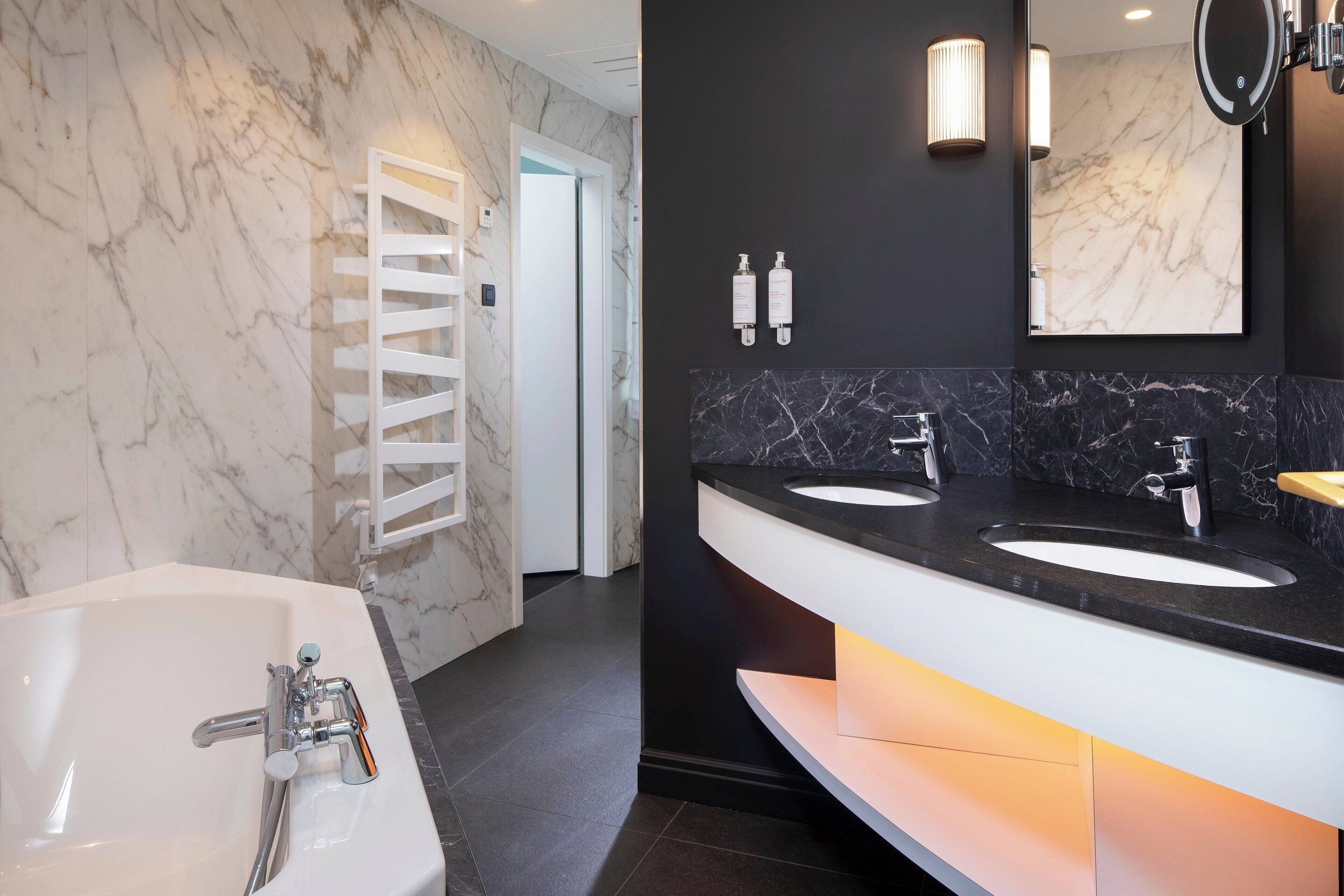 A modern bathroom with a white bathtub, two sinks with black countertops, and marble walls.