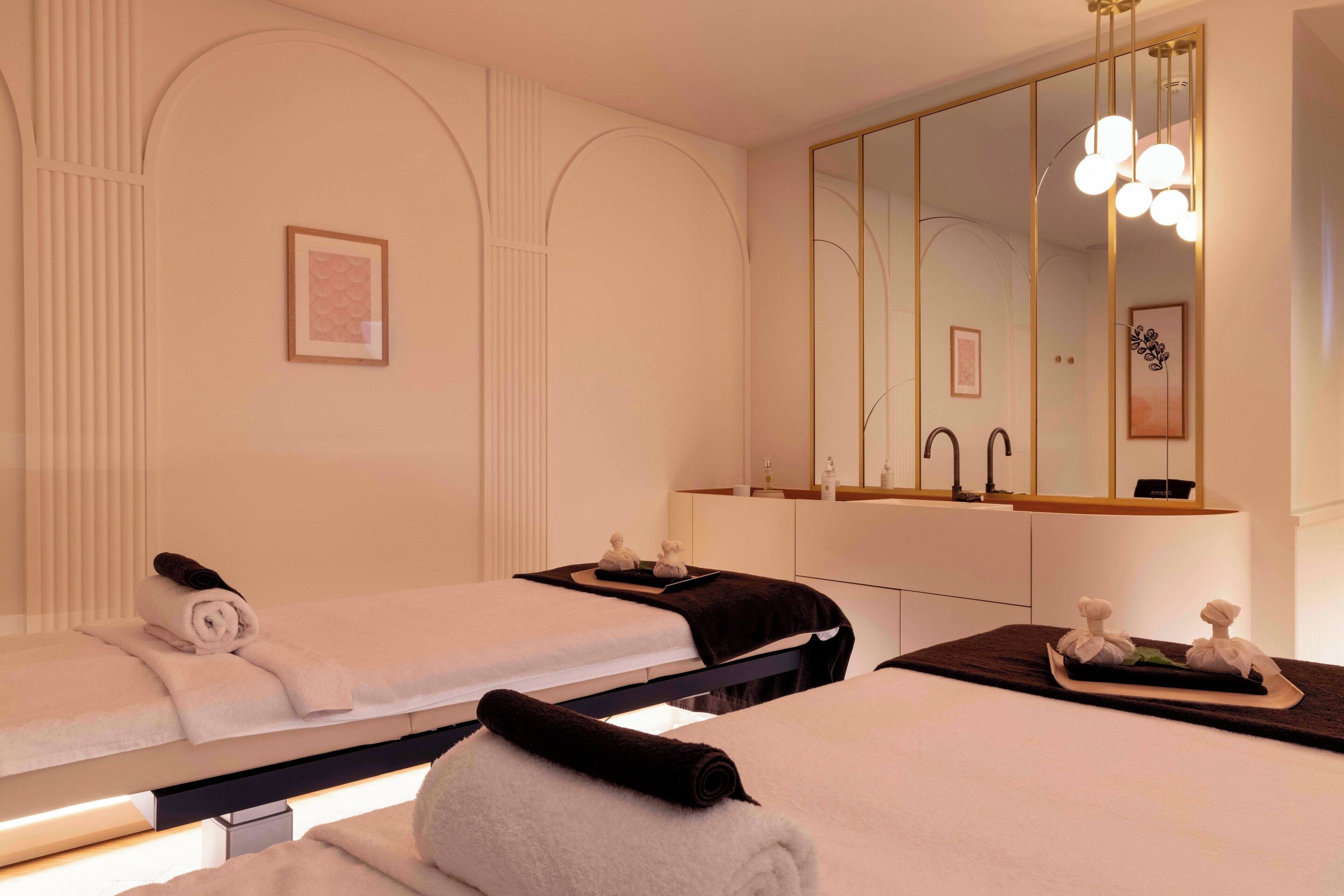 A spa room with two beds, a large mirror, and a tray with towels and toiletries.