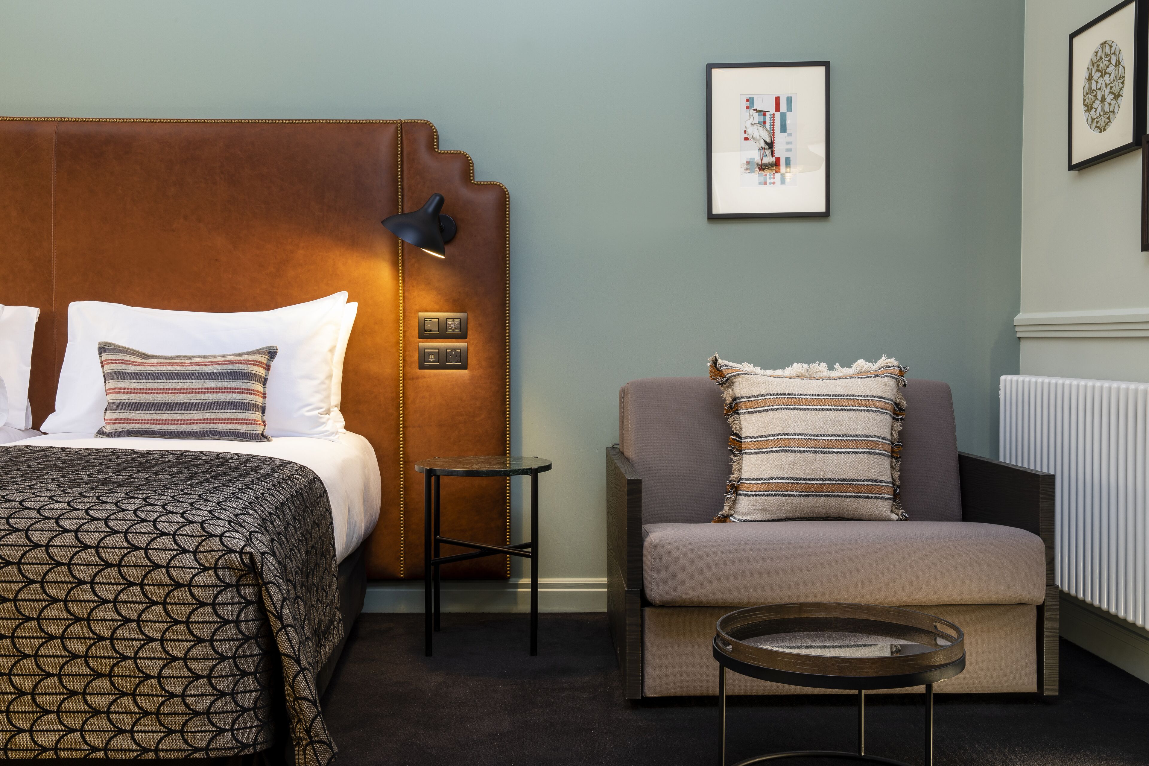 A hotel room with a large bed, a sofa, a small table, and a wall-mounted lamp.