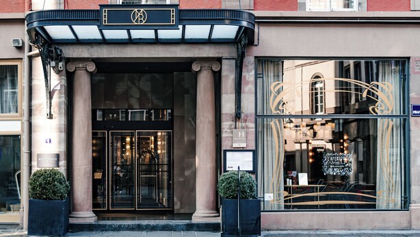 A hotel entrance with a black awning, large glass windows, and a balcony with flowers. - Maison Rouge Strasbourg Hotel&Spa, Autograph Collection (Strasbourg)
