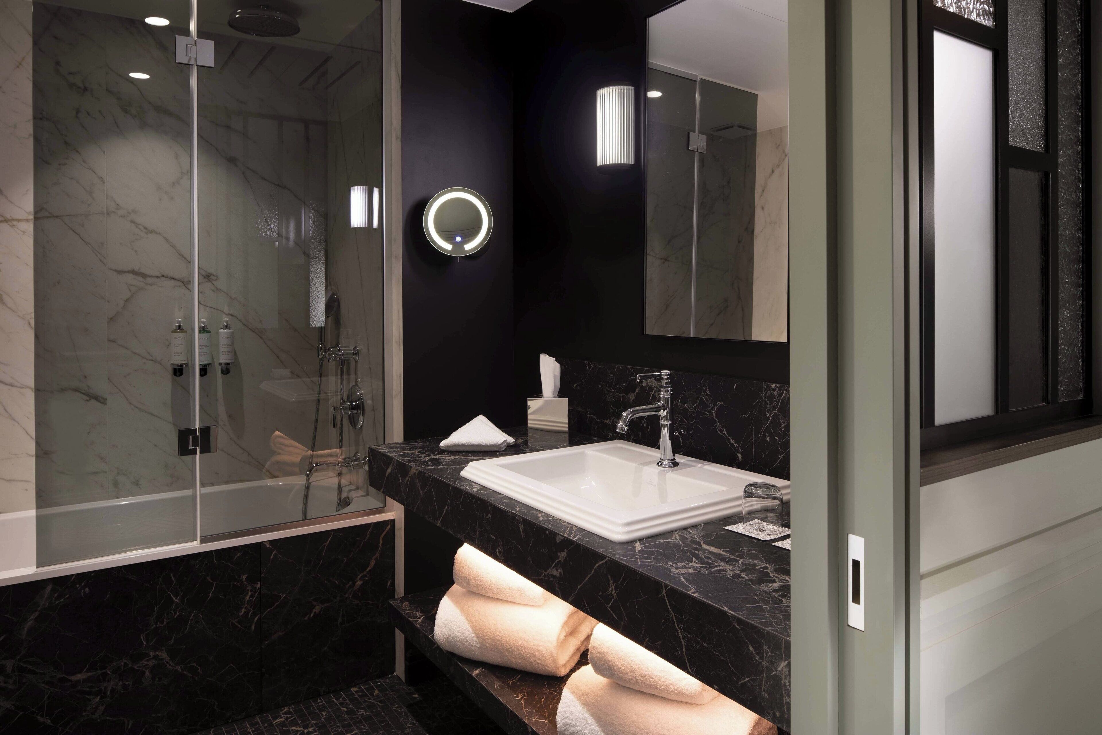 A modern bathroom with a glass-enclosed shower, a white sink, and a large mirror.