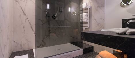 A modern bathroom with a glass-enclosed shower, marble walls, and a black countertop with a towel rack.