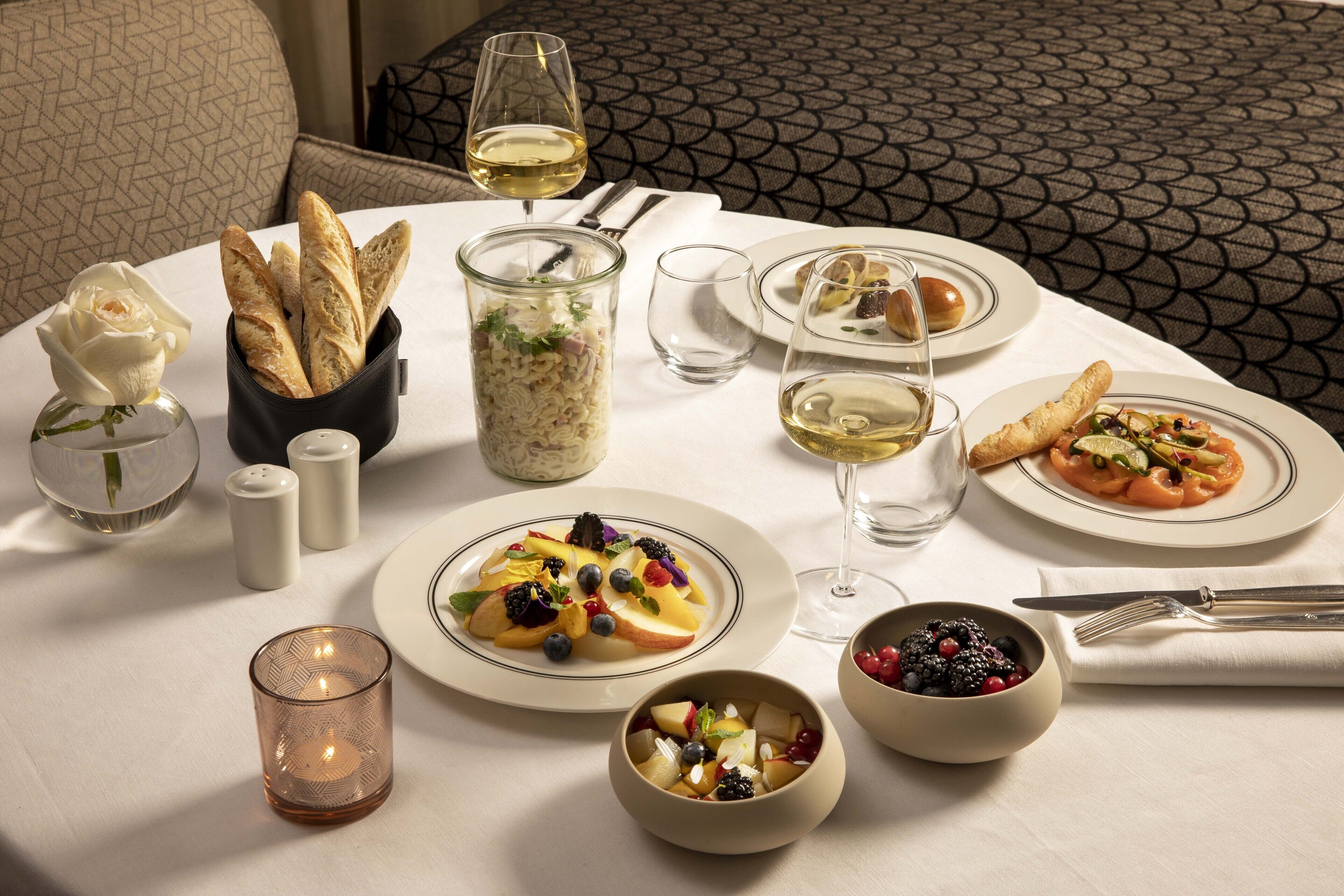 Une table à manger dressée avec des assiettes remplies de nourriture, des verres de vin et une bougie.