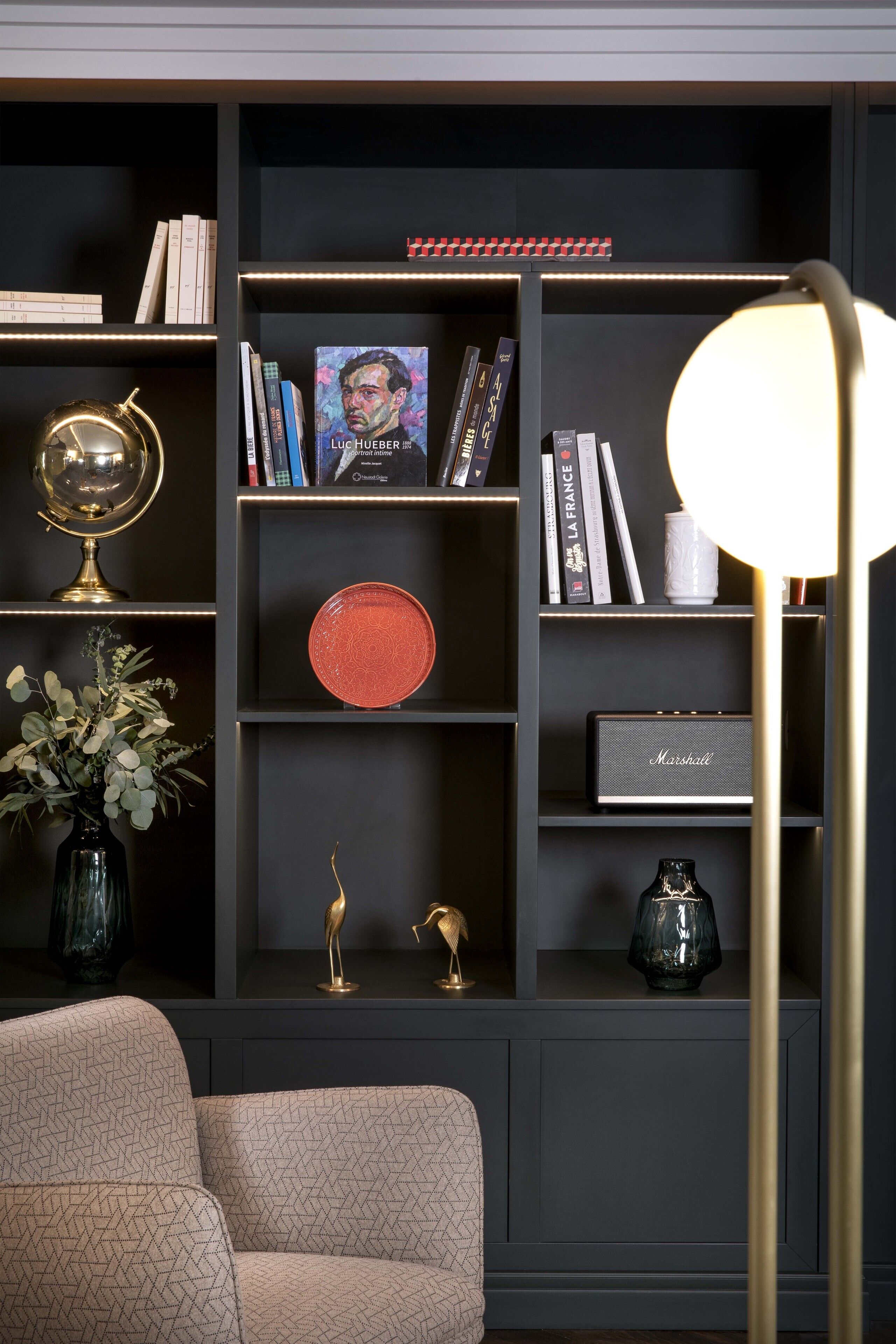 Uma estante escura com livros, objetos decorativos e um aparelho Marshall.