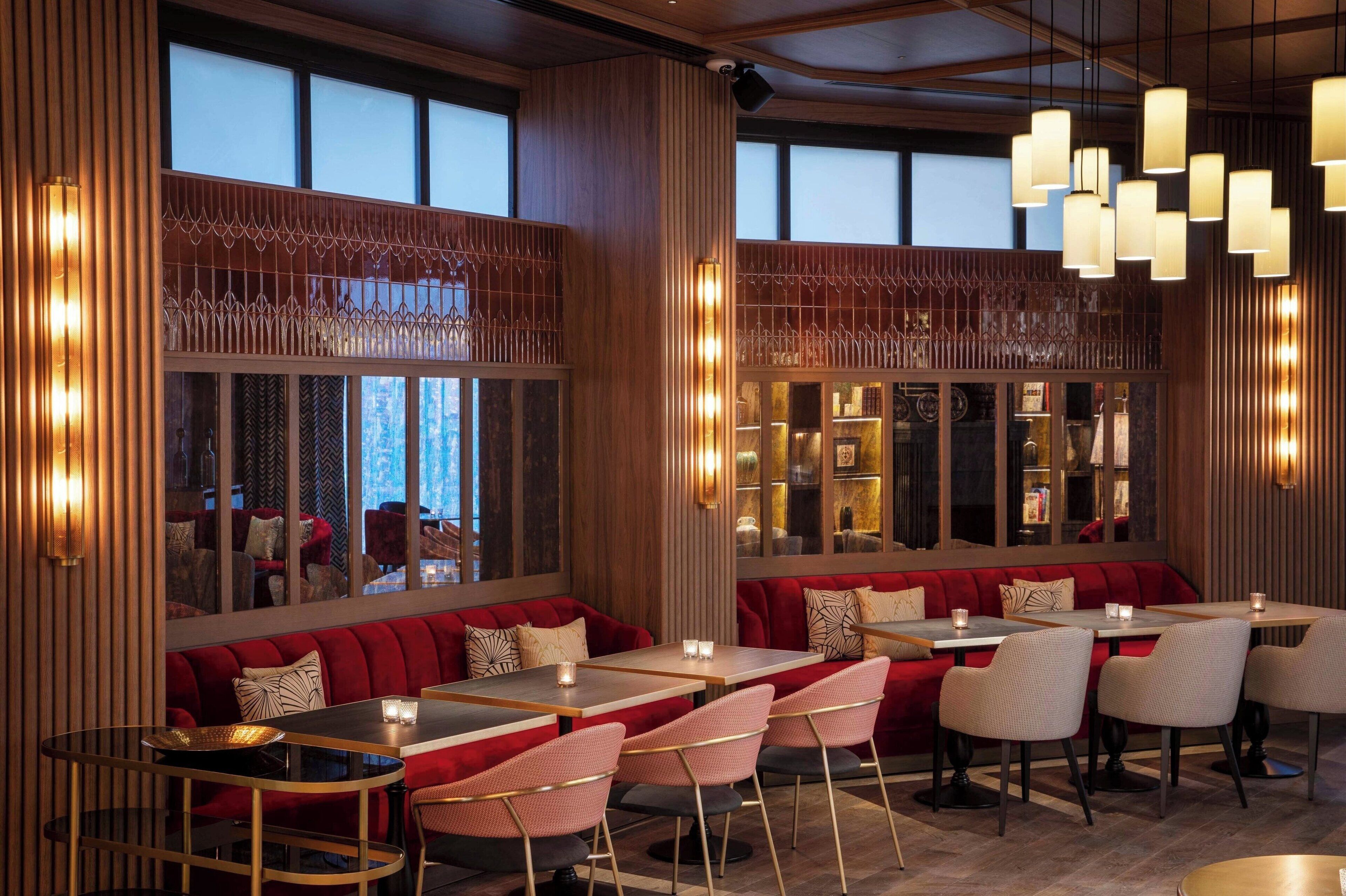 Interior de restaurante con asientos tapizados en rojo, paneles de madera e iluminación colgante.
