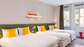 Een hotelkamer met twee bedden, een groen hoofdeinde en een raam met uitzicht op gebouwen.