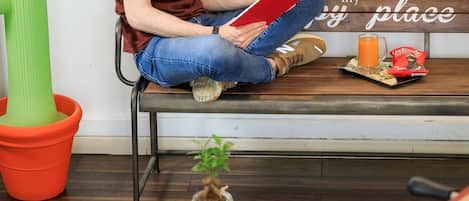 A man sitting on a bench reading a book, with a foosball table and a cactus in the room.