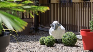 A garden area with a decorative sheep statue, two spherical topiary bushes, and a red potted plant.