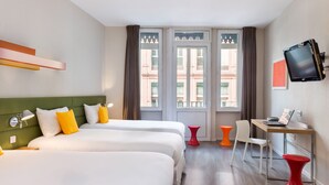 A hotel room with two beds, a desk, a chair, a TV, and a window with curtains.
