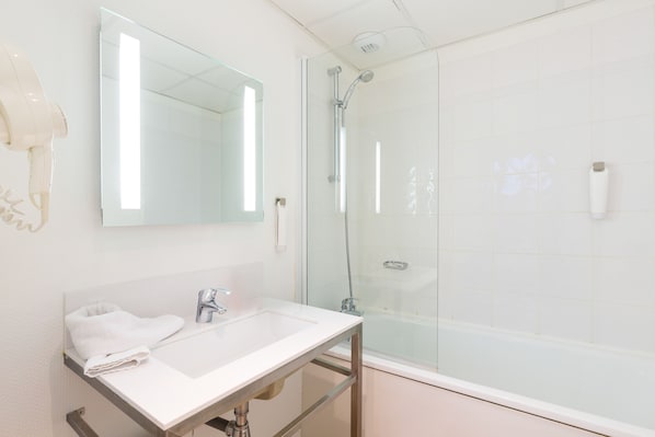 Un baño con lavamanos blanco, espejo, ducha con mampara de vidrio y bañera blanca.
