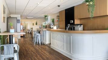 A modern cafe with a wooden counter, metal chairs, and hanging plants.