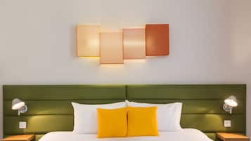 Een net opgemaakt bed met witte en gele kussens, een groen gestoffeerd hoofdeinde en twee nachtkastjes met lampen.