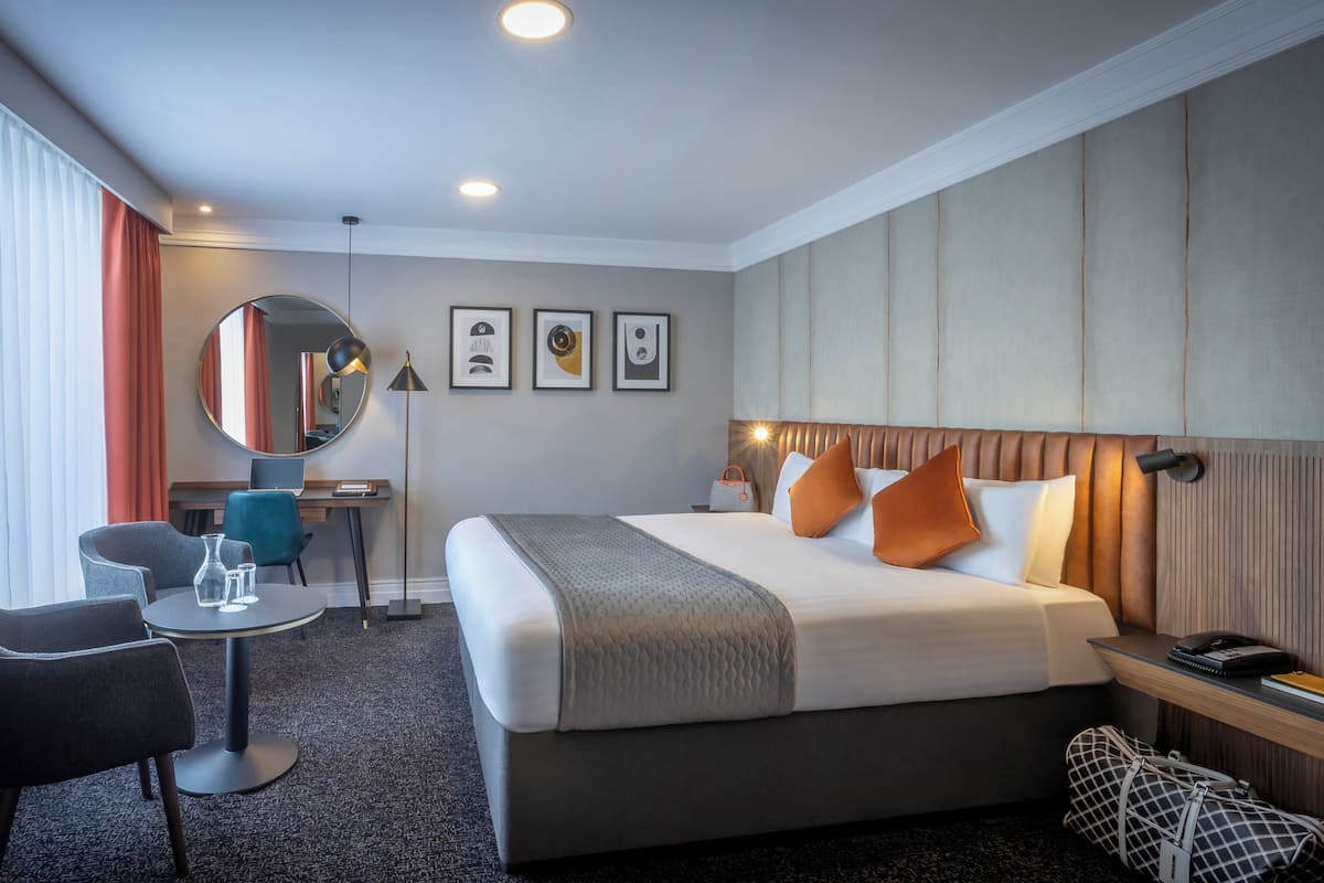 A hotel room with a bed, a desk, a chair, a round table, and a mirror.