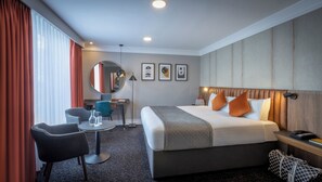 A hotel room with a bed, a desk, a chair, a round table, and a mirror.