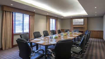 Un salón de conferencias con una larga mesa, sillas negras y una pantalla de televisión que muestra 'Talbot Hotel Stillorgan'.
